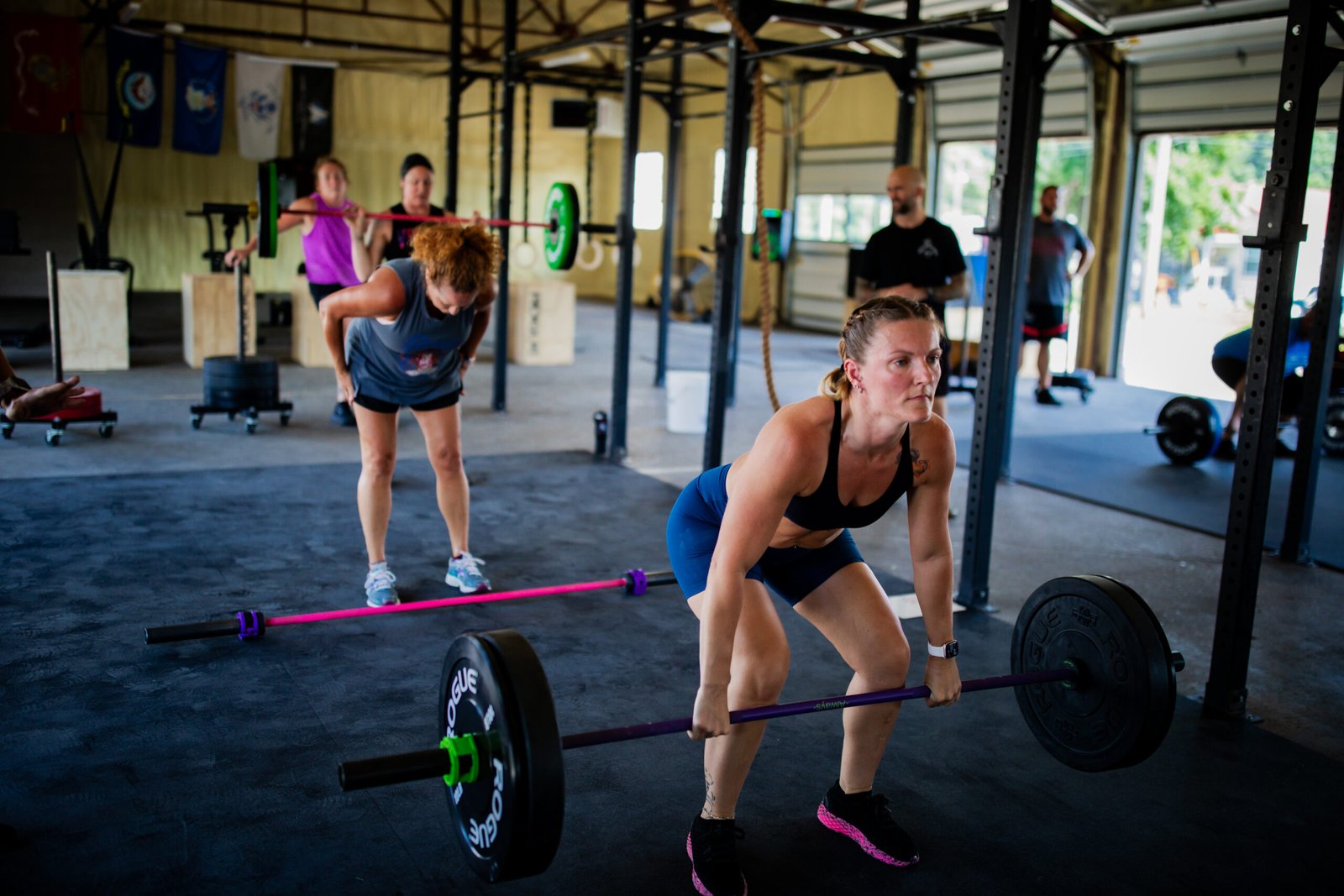 Woman performing power clean during a CrossFit class at Arc Reactor CrossFit in Zanesville, while others train in the background.